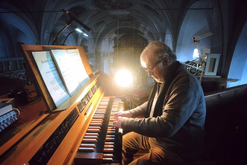 Een man met een bril en met een dikke trui aan bespeelt in een klooster in het Duitse Gars am Inn een orgel.