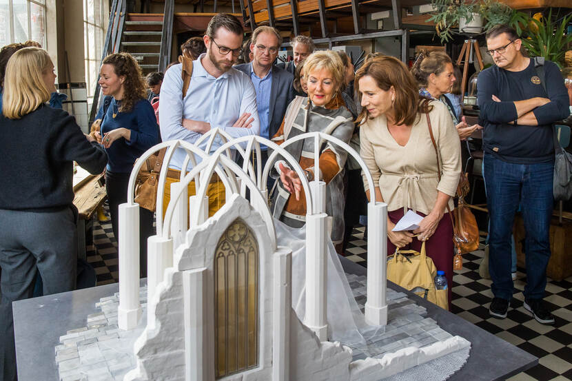 Mensen staan om een witte maquette heen met grote witte bogen, de contouren van een kerkgebouw.